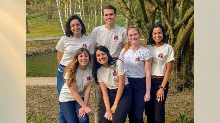PhD Committee six PhD committee members wearing matching white shirts standing on a grassy area with trees in the background